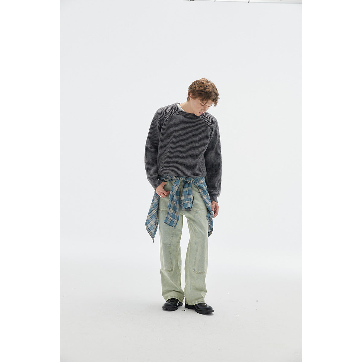 Full-length model wearing a charcoal ribbed raglan sweater with pale green jeans and a blue plaid shirt tied at the waist.