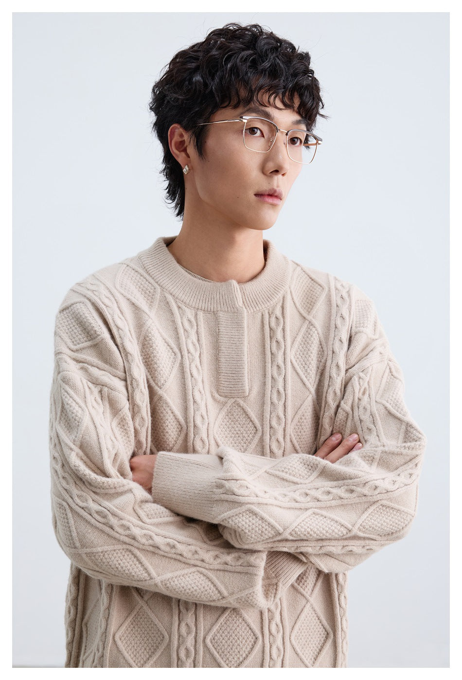 Close view of a model wearing a cream cable-knit sweater with raised diamond, braided and textured panels.