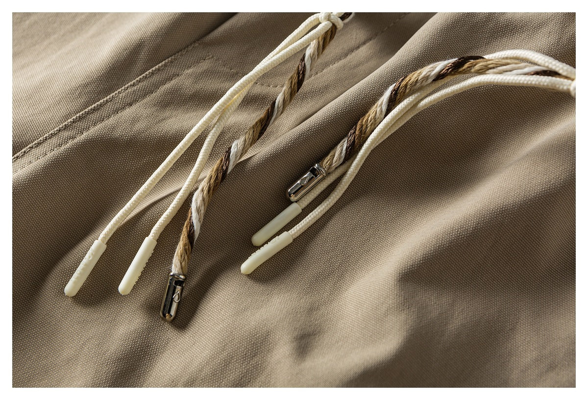 Close-up of khaki shorts showing braided drawstring ends with metal fittings and pale tips.