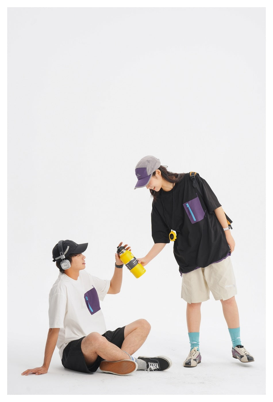 Two models wear oversized tees with contrasting zip chest pockets: black with purple trim and white with purple trim.