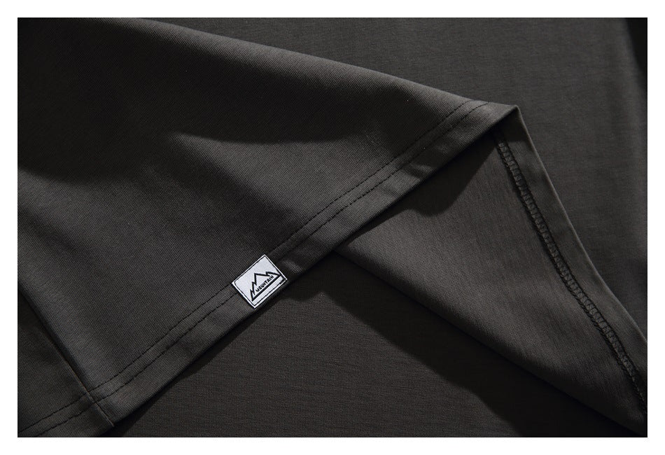 Close-up of a dark charcoal T-shirt sleeve hem with a small mountain patch and visible seam stitching.