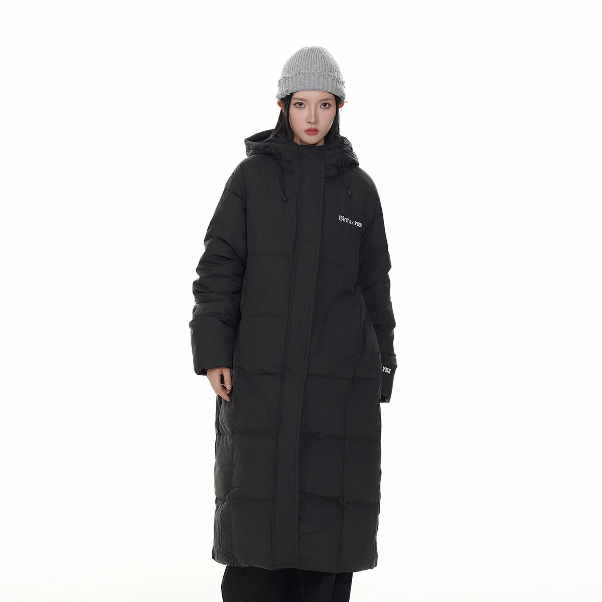 Front view of a model in a long black hooded puffer coat and gray knit beanie.