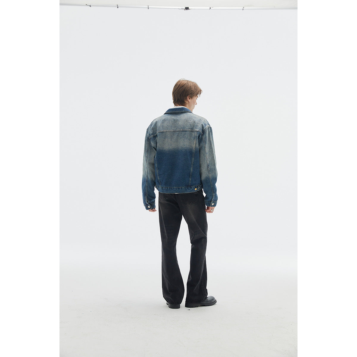 Rear view of a model wearing a faded blue denim jacket with a dark blue back panel and black wide-leg pants.
