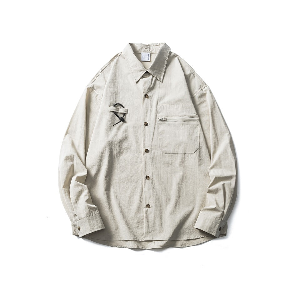 Beige long-sleeve button-up shirt with zippered chest pocket and beaded loop detail, flat lay front view