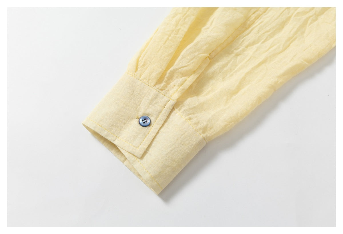 Close-up of a pale yellow shirt sleeve cuff with a small blue button and stitched seams.