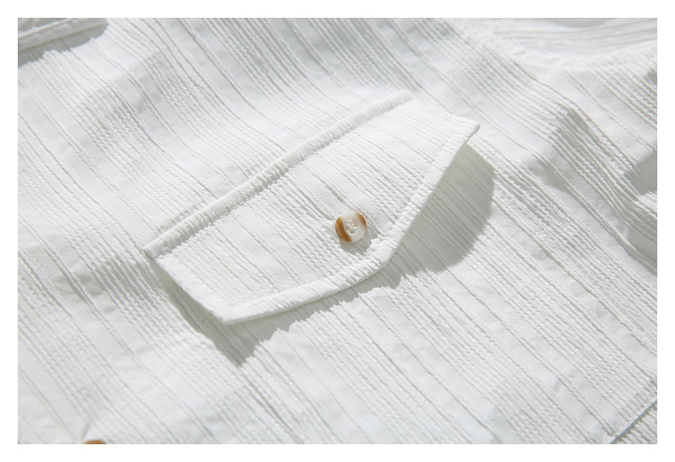 Close-up of a white shirt's textured fabric and buttoned chest pocket.
