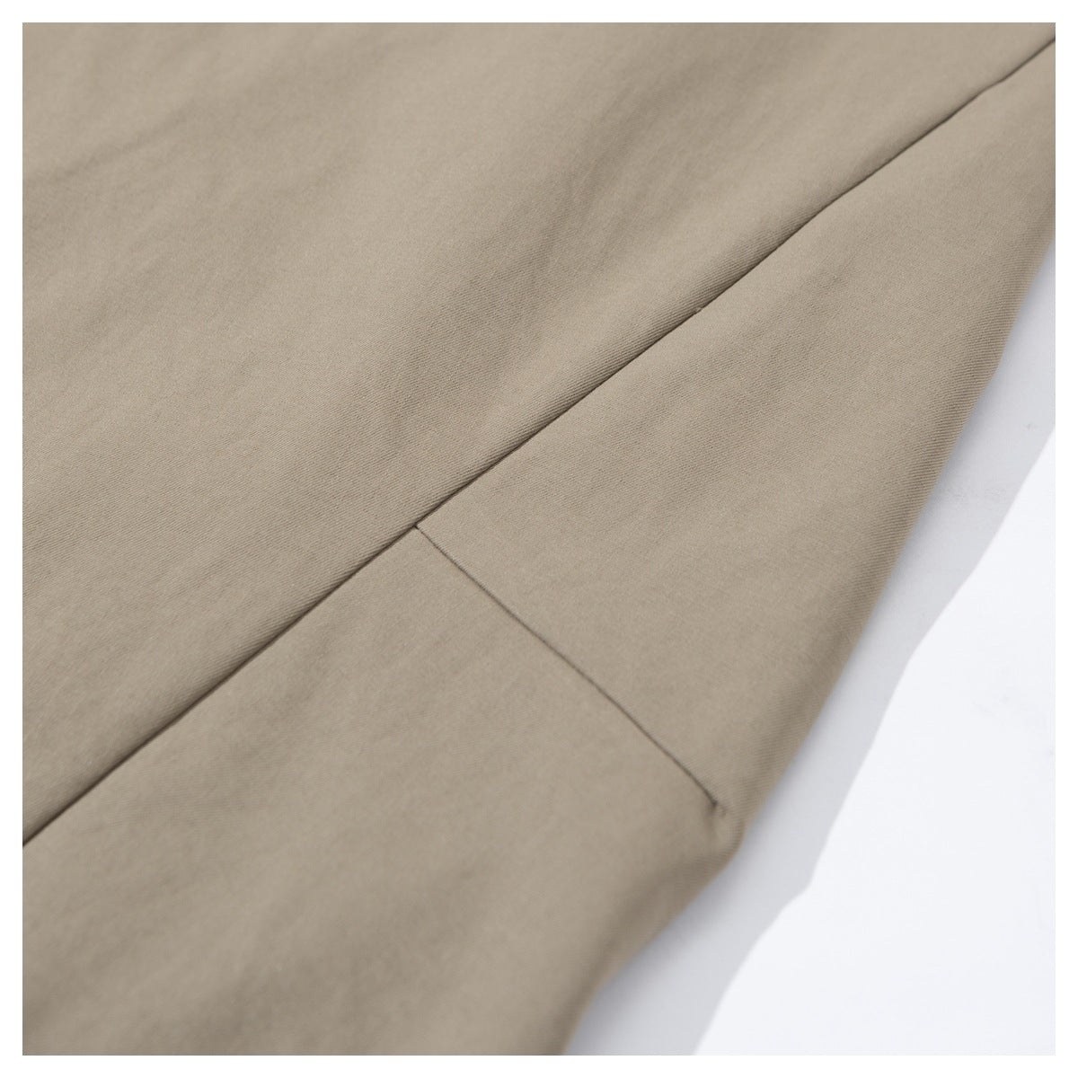 Close-up of taupe trouser fabric and a stitched seam along a folded leg.