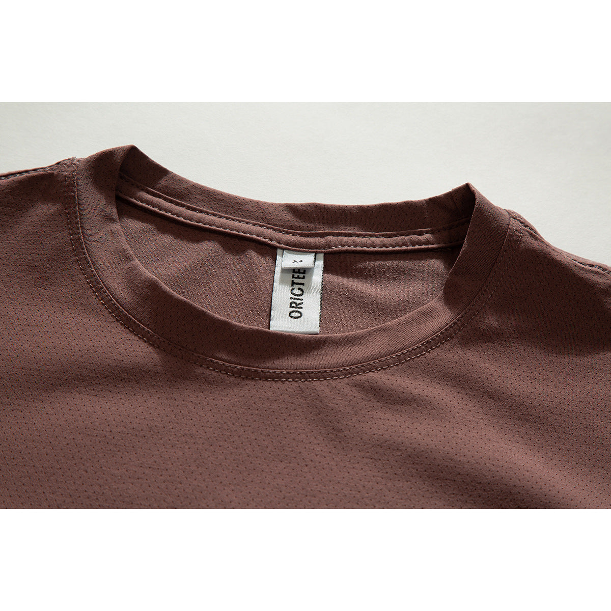Close-up of a brown perforated crew-neck shirt showing the collar stitching and white neck label.