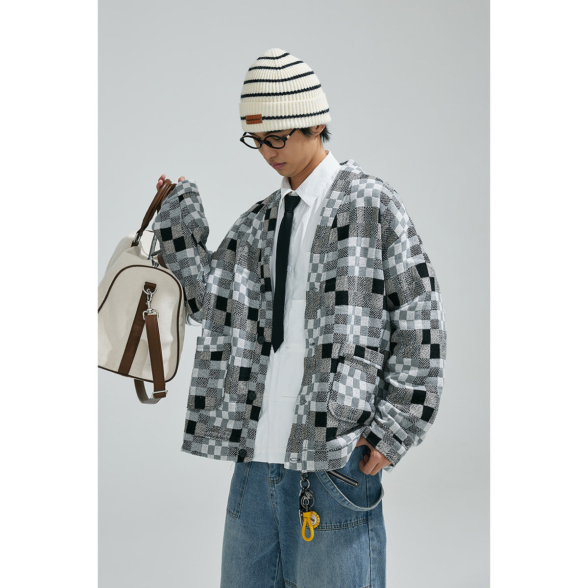 Closer view of a model wearing a black, gray and white patchwork-check cardigan with front buttons and patch pockets.