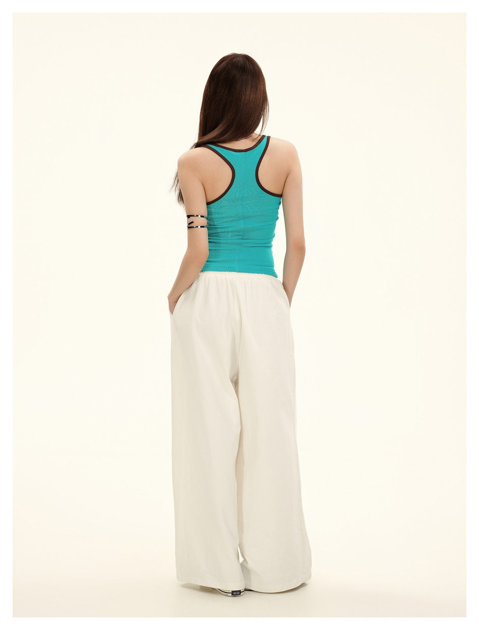 Back view of a model wearing a turquoise racerback tank with dark trim and loose white wide-leg pants.