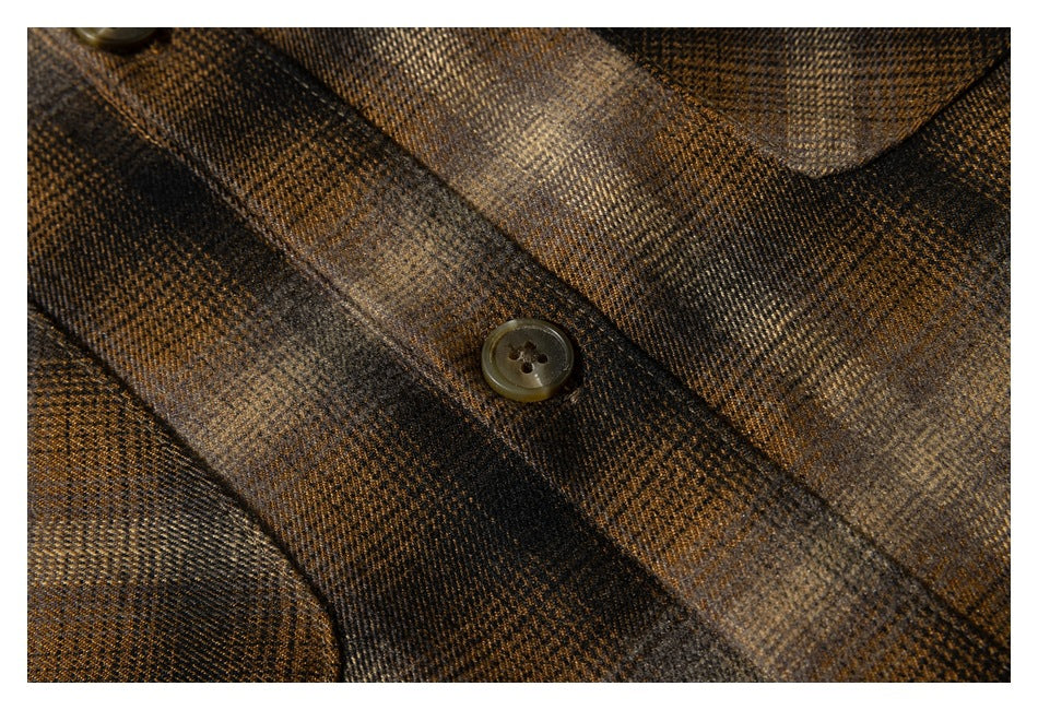 Close-up of a brown button and the shirt's brown, black, and tan plaid fabric.