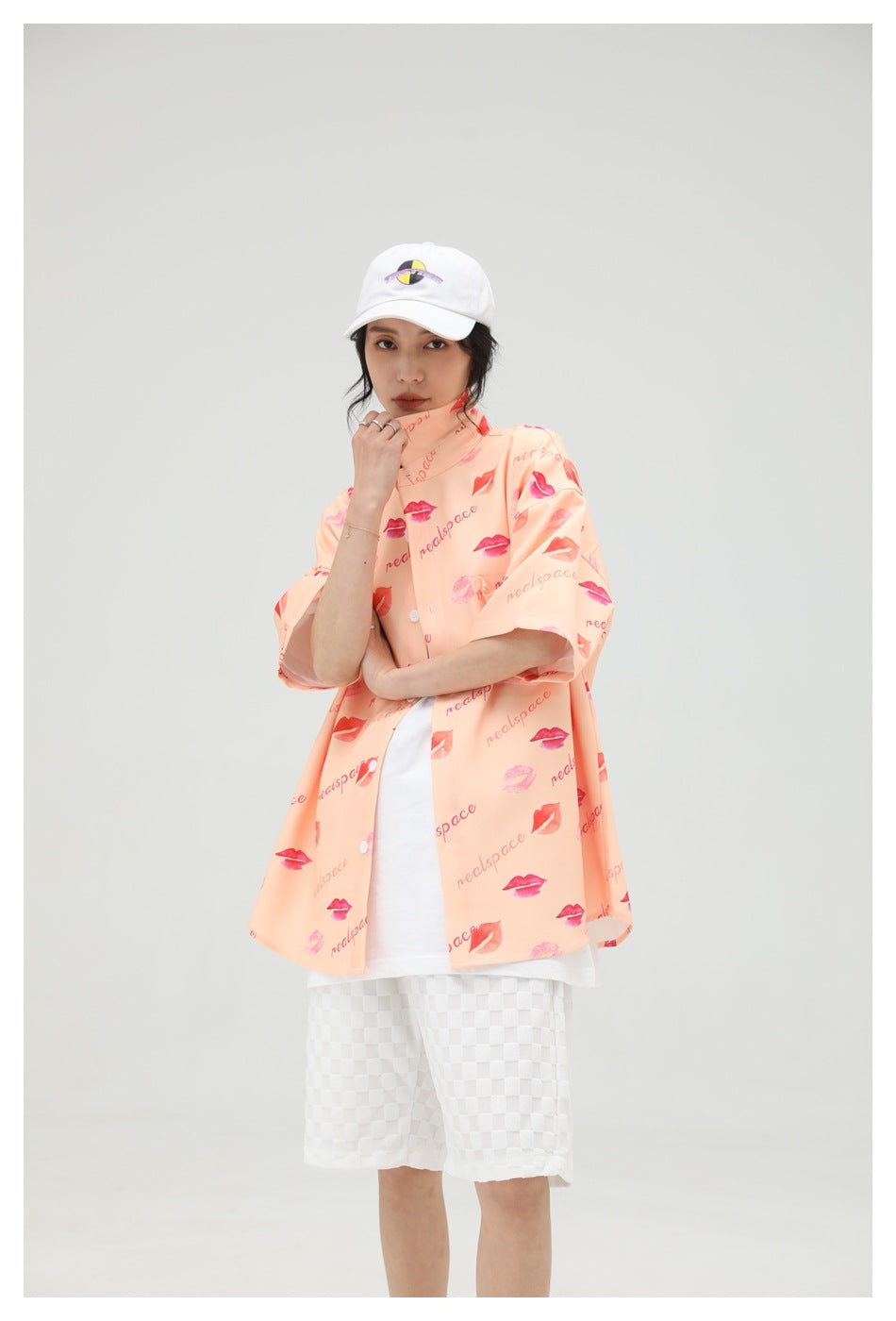 Model wearing the peach lip-print button-up shirt open over a white top with white checkered shorts.