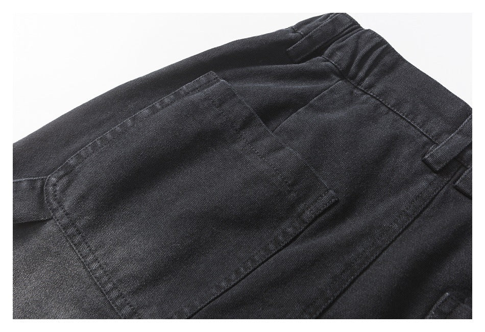Close-up of a stitched patch pocket and waistband on black textured trousers.