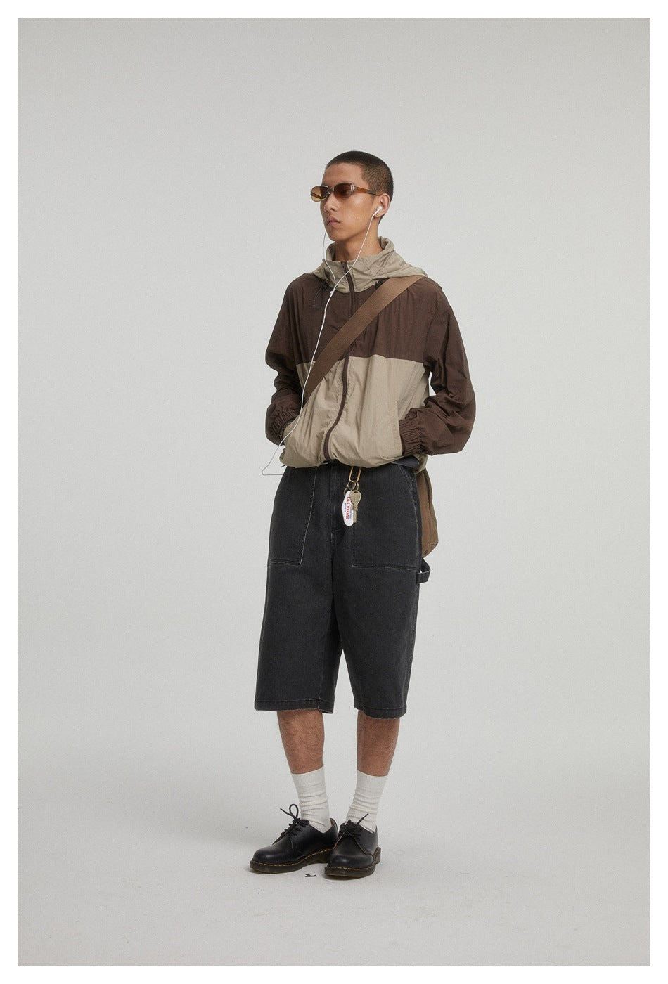 Model wearing a brown and beige hooded color-block jacket with black knee-length shorts.