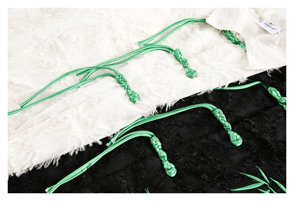 Close-up of braided green tie closures on ivory and black shirts with fringed geometric fabric.