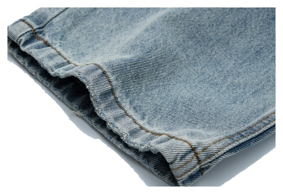 Close-up of the hem and orange-brown stitching on light-wash denim jeans.