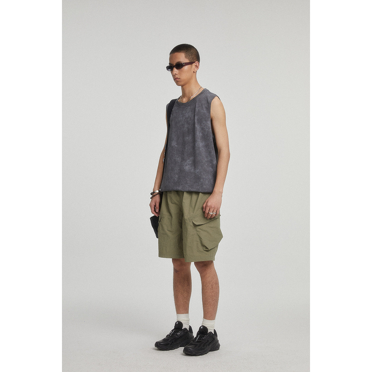 Three-quarter view of a man in a charcoal sleeveless top and olive cargo shorts.