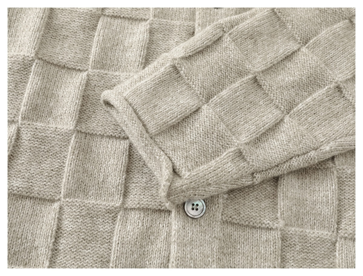 Close-up of a sleeve laid across the light beige cardigan, showing the textured knit and cuff edge.
