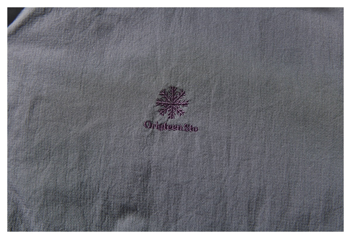 Close-up of a purple embroidered snowflake and lettering on charcoal gray jacket fabric.