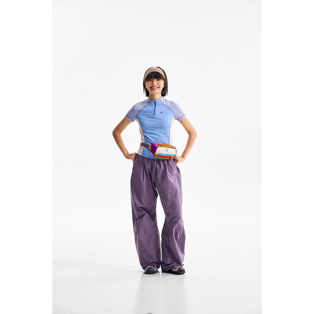 Model wearing a blue and lavender short-sleeve zip-neck top with loose purple pants.