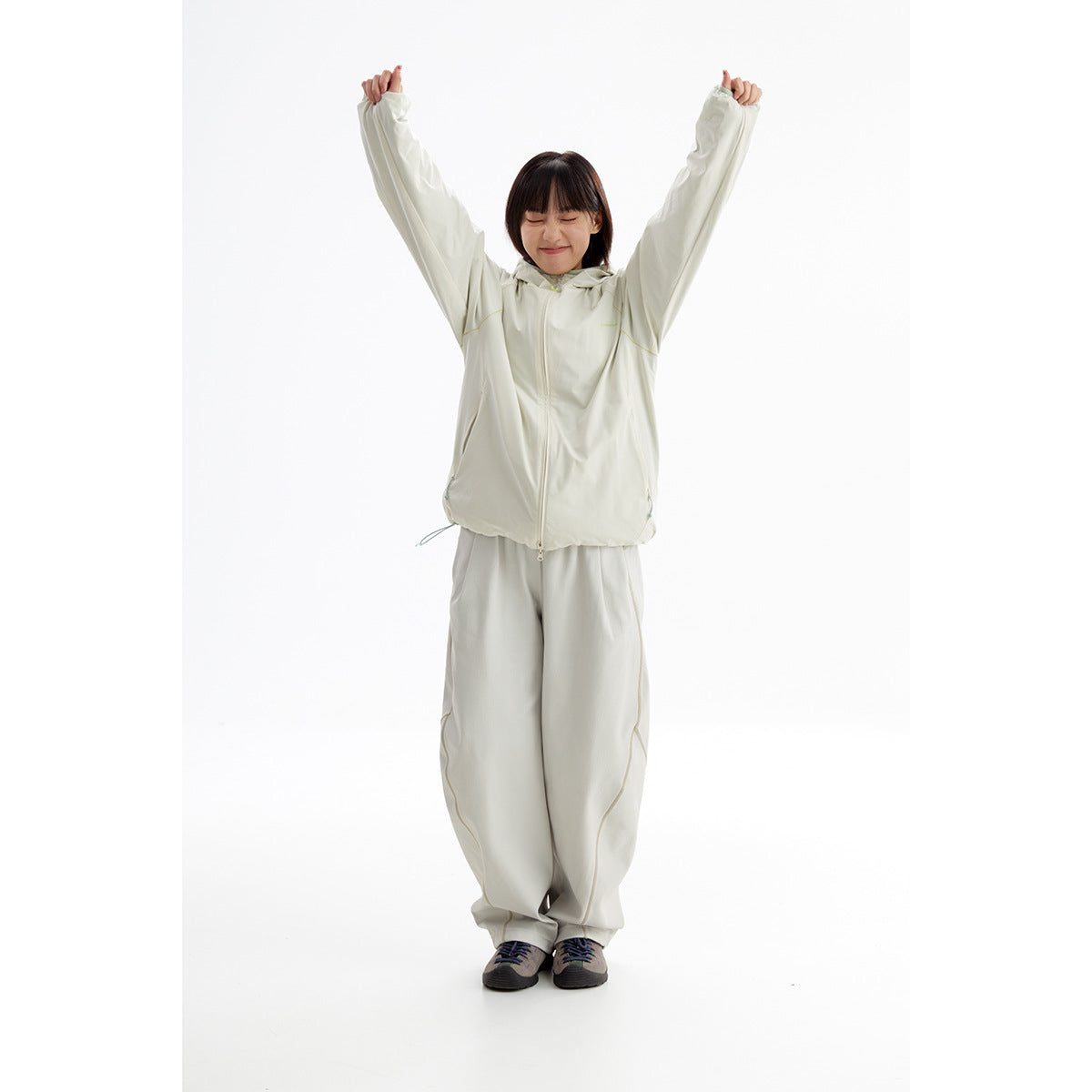 Model in a light gray hooded zip jacket and matching loose trousers, posing with arms raised.
