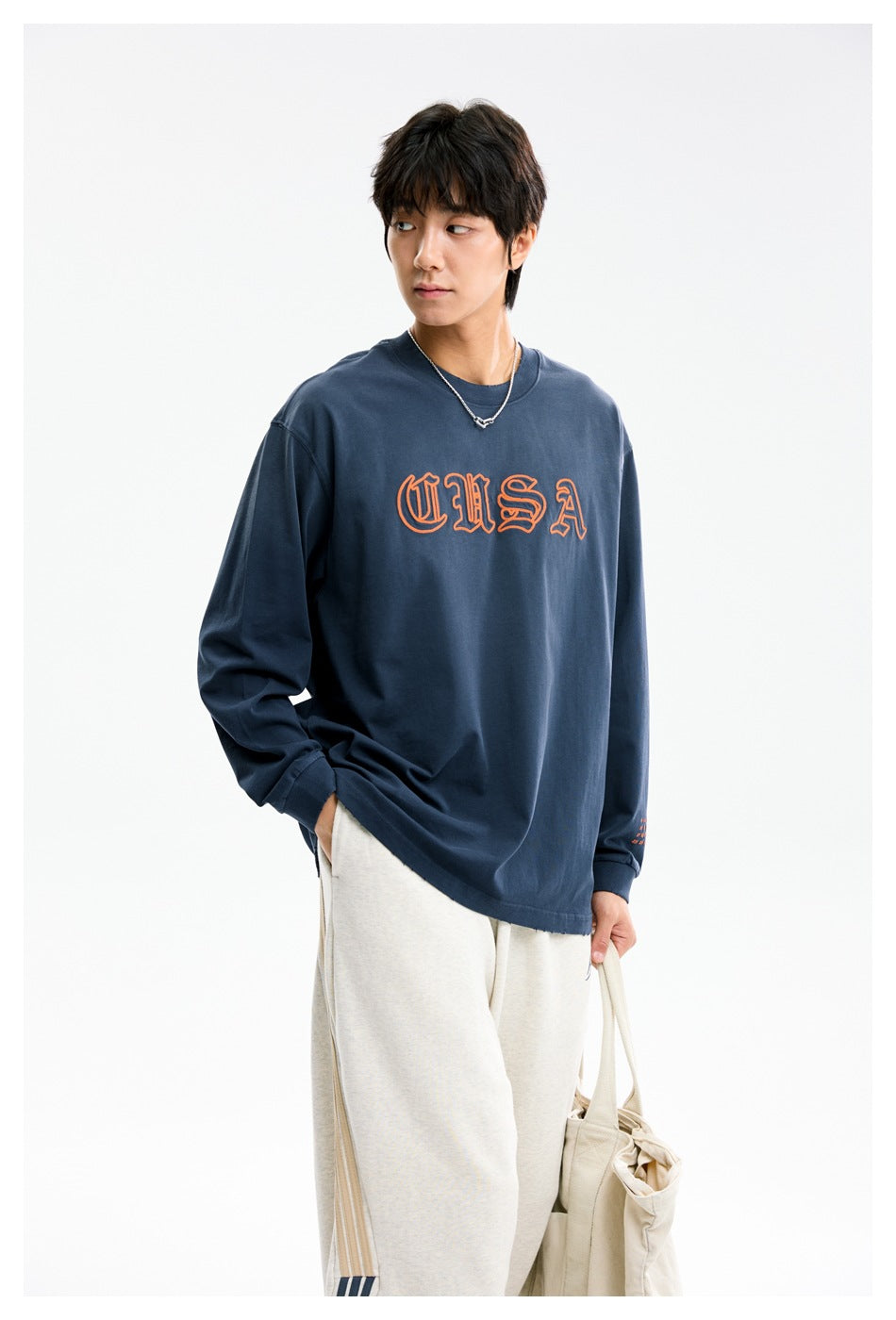 Model wearing a navy long-sleeve shirt with orange outlined lettering, shown at a slight angle.