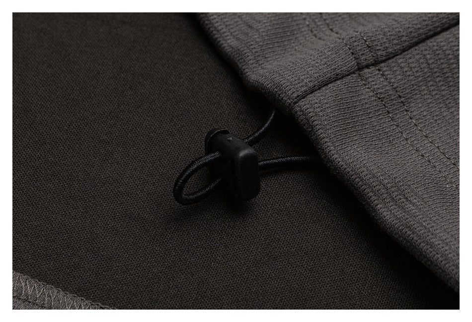 Close-up of a black drawcord toggle beside a ribbed charcoal garment edge.