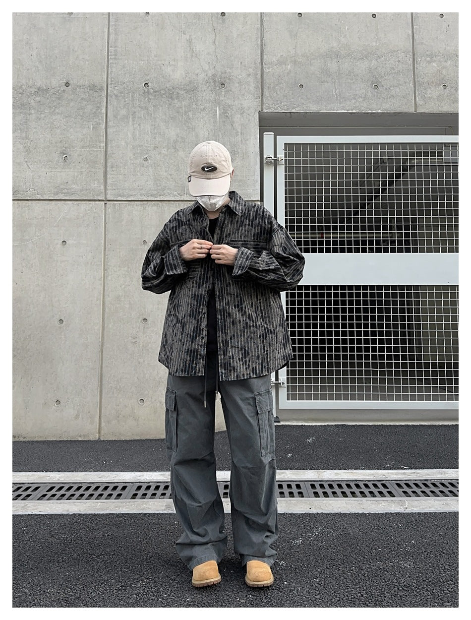 Full-length model wearing a charcoal distressed-stripe button-up shirt, gray cargo pants, and tan boots against a concrete