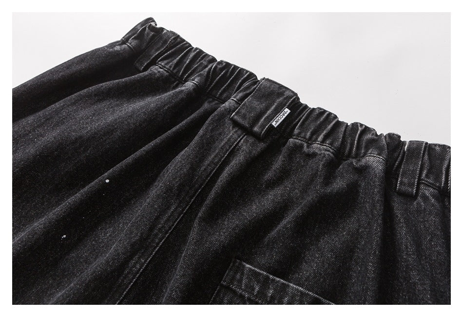 Close-up of black denim trousers with a gathered elastic waistband, belt loops and pocket edge.