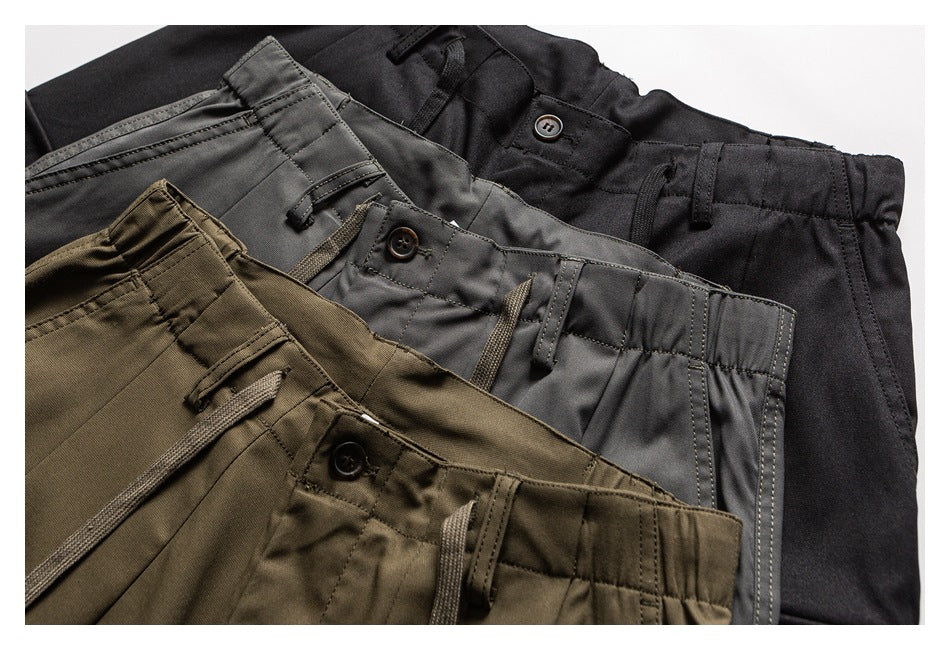 Three pairs of trousers in black, charcoal gray, and olive, arranged overlapping to show their waistbands and drawstrings.