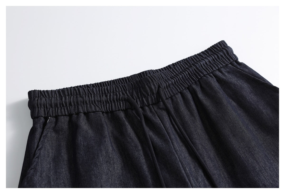 Close-up of dark indigo pants with a gathered elastic waist and a dark drawstring.