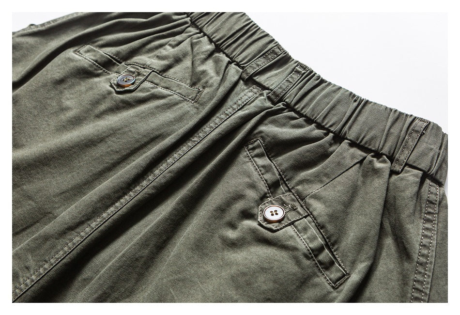 Olive trousers shown close up at the front, with an elastic waist, pleats and buttoned pockets.