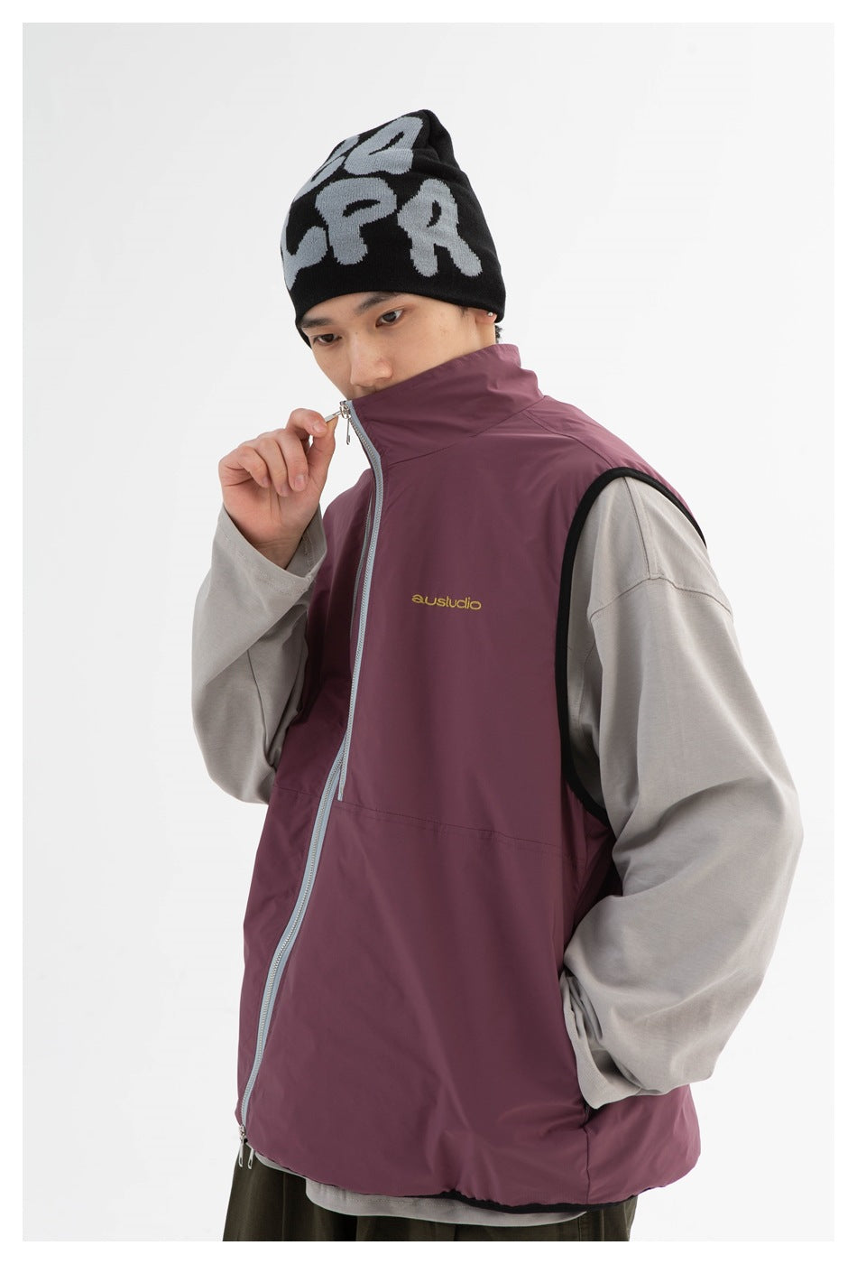 Model wearing a plum sleeveless zip vest over a gray top, with a high collar and gold chest embroidery.