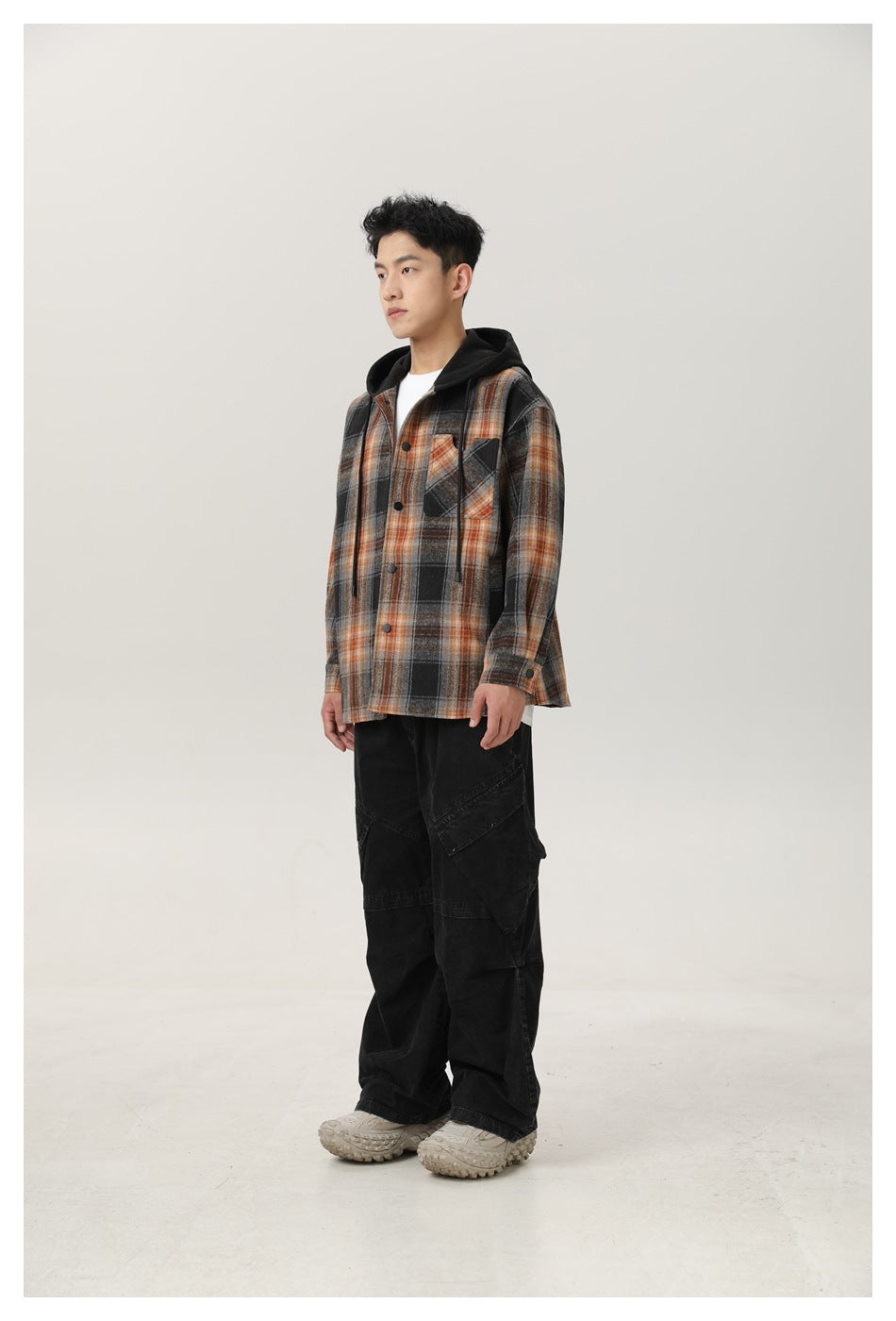 Man wearing the plaid hooded jacket over a white tee with black cargo pants, standing in a three-quarter side view