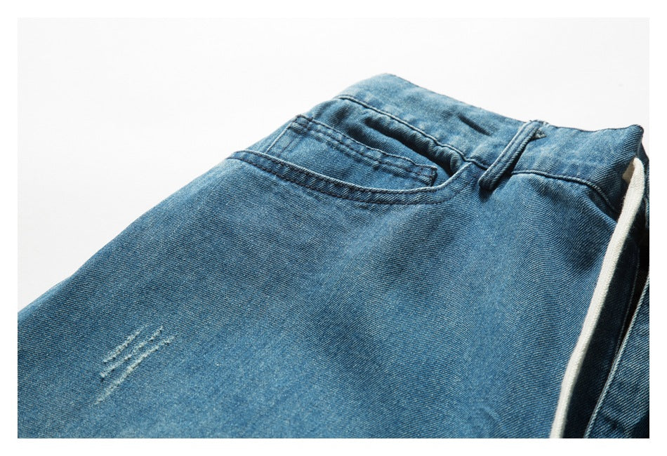 Close-up of blue denim bottoms showing the waistband, a pocket, small distressed slashes and a white drawstring.