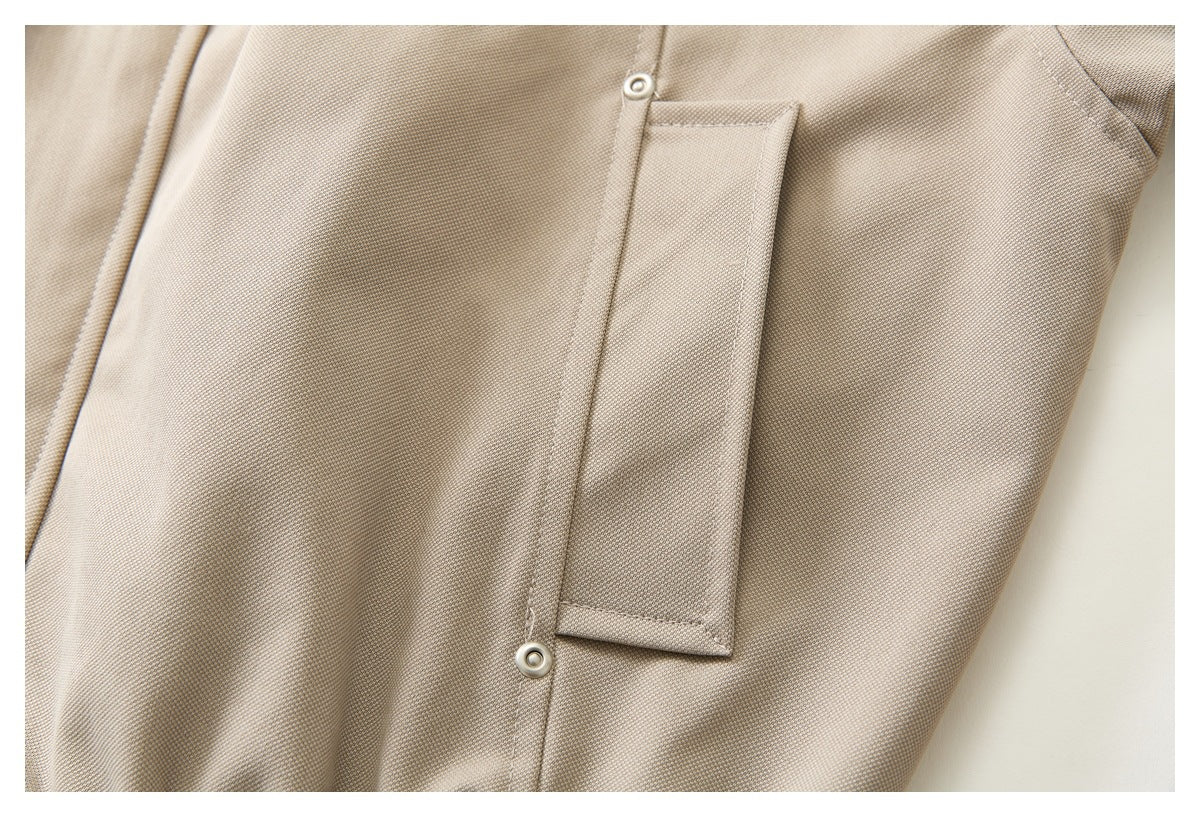 Close-up of a narrow beige jacket pocket with two metal snaps.