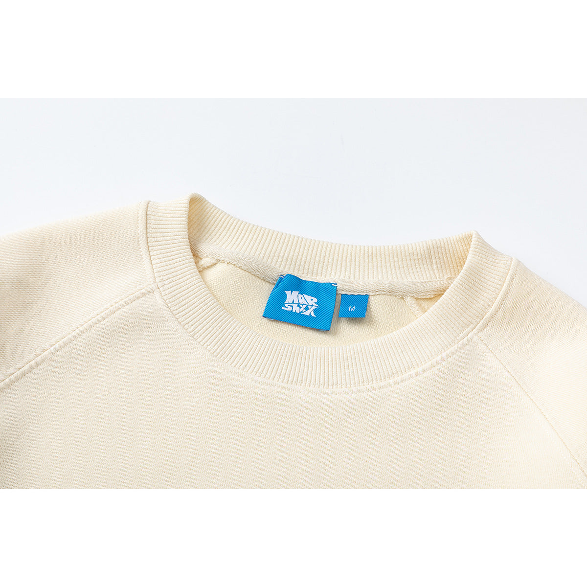 Close-up of a cream sweatshirt's ribbed crew neckline and blue size and brand tags.