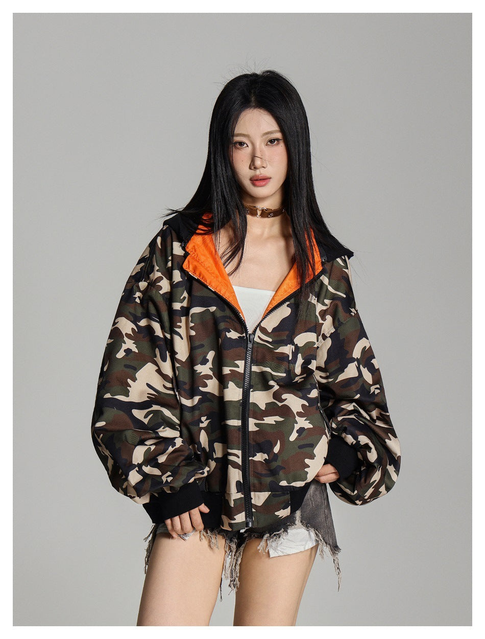 Model wearing a front-zip camouflage jacket with orange lining, black hood and cuffs, and voluminous sleeves.