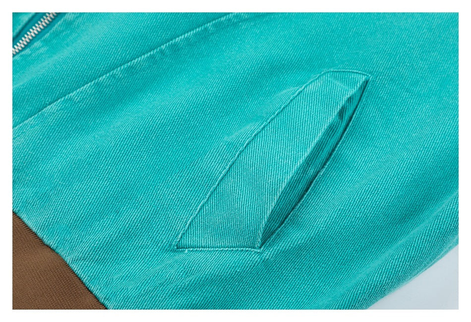 Close-up of a slanted welt pocket on turquoise jacket fabric, with a brown ribbed edge visible.