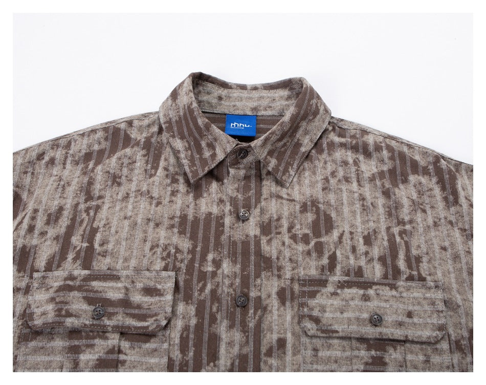 Close-up of a taupe patterned shirt front, showing its collar, button placket, and two flap chest pockets.