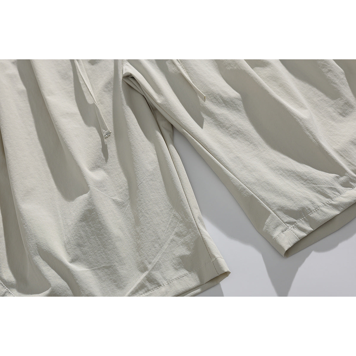 Close-up of light beige shorts showing the drawstring, leg seams, and stitched hems.