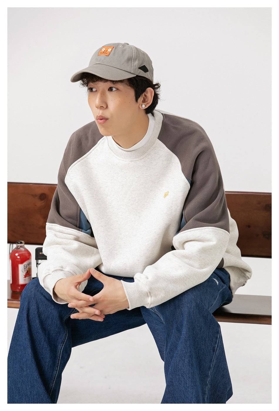 Seated model wearing an oatmeal, charcoal, and blue color-block raglan crewneck sweatshirt.