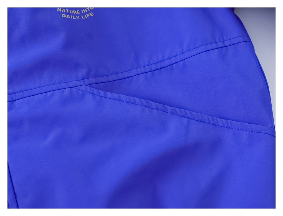 Close-up of a vivid blue garment with curved stitched seams and small gold “NATURE INTO DAILY LIFE” lettering.