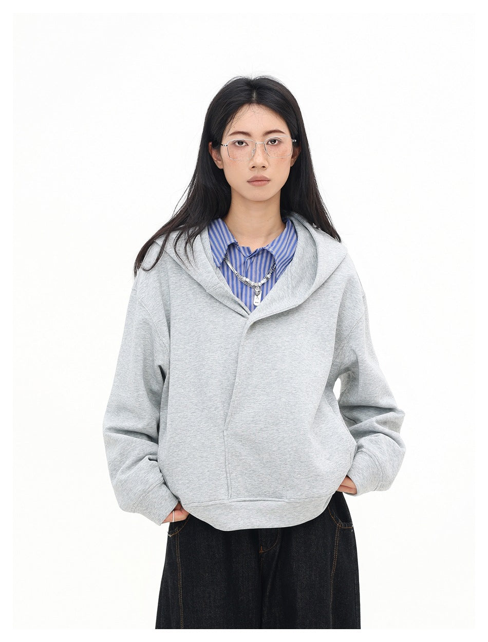 Front view of a model wearing a light gray oversized hooded sweatshirt over a blue striped shirt and dark jeans.