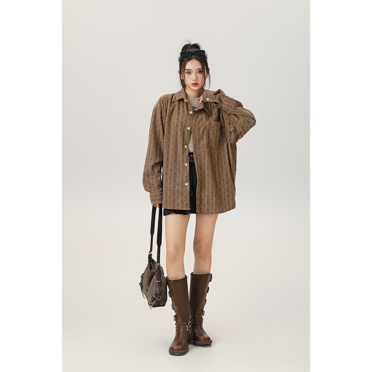 Model wearing an oversized brown patterned button-up shirt with black shorts and tall brown boots, front view.