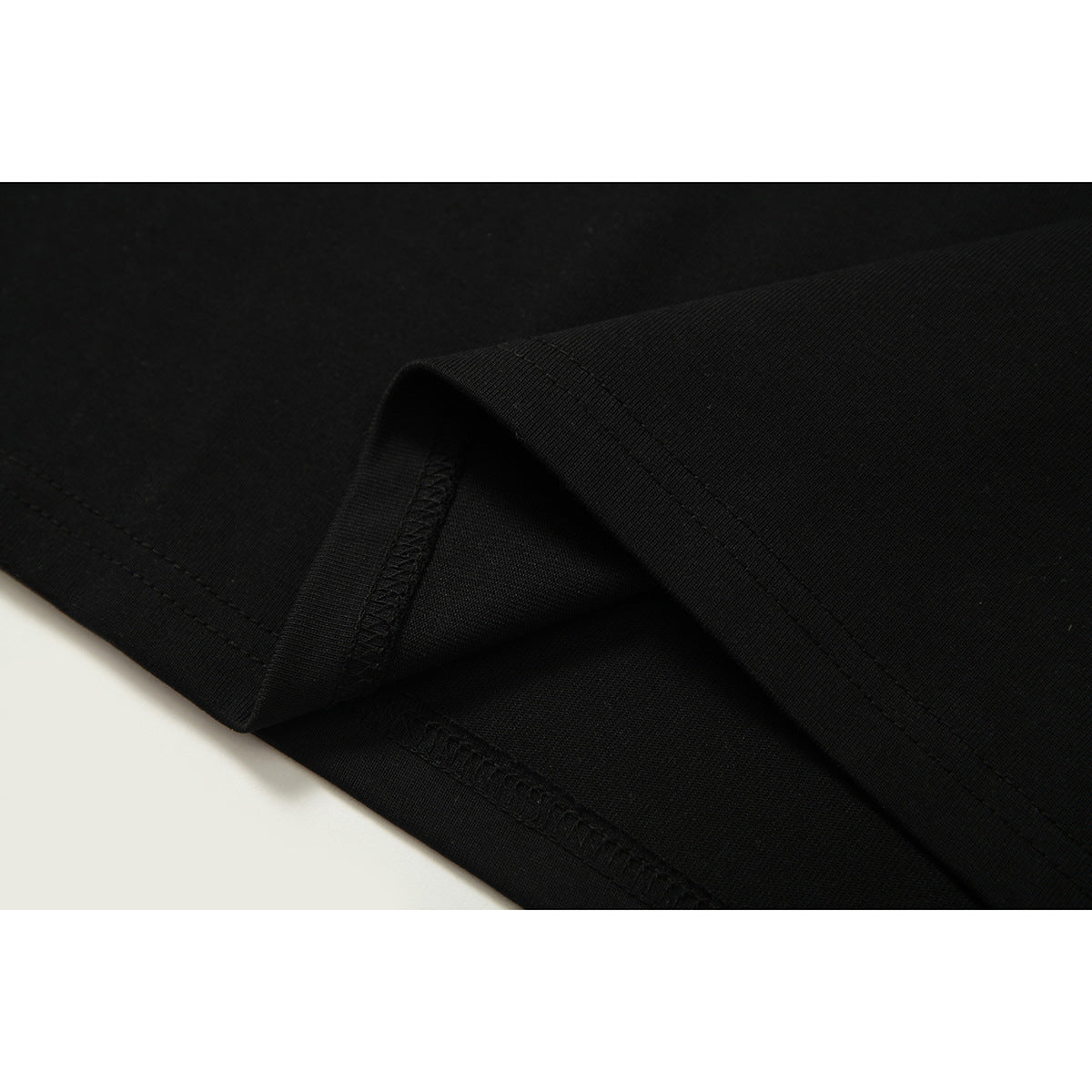 Close-up of black T-shirt fabric folded to show the hem stitching and inside seam.