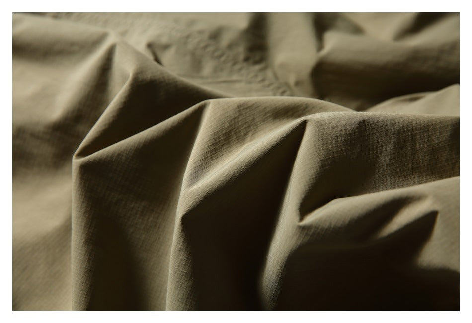 Extreme close-up of olive-khaki shorts fabric gathered into folds, showing its fine grid-like texture.