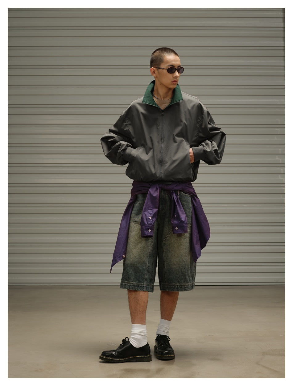 Model wearing a charcoal zip jacket with a dark green collar and a purple jacket tied over faded denim shorts.