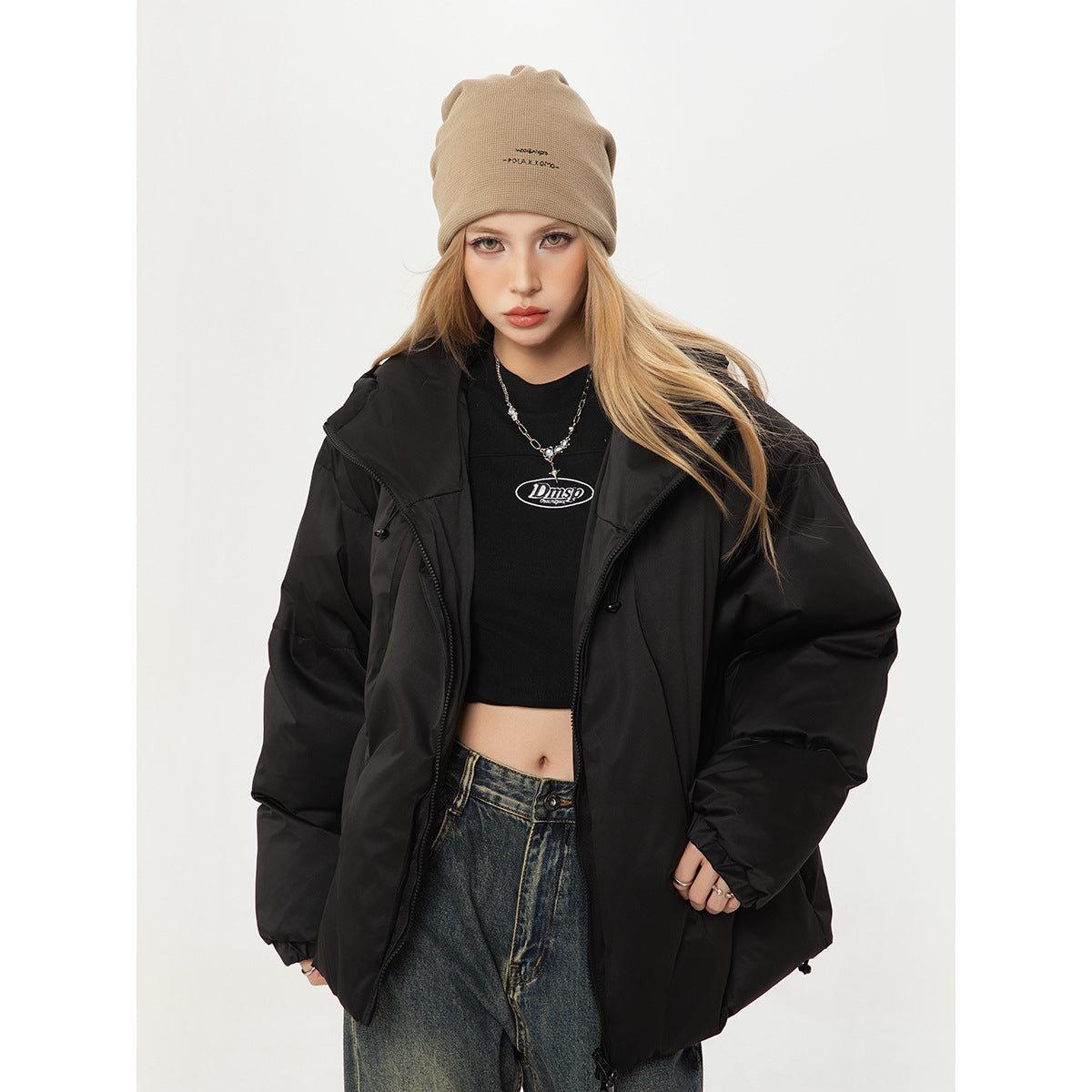 Closer view of a model in an open black puffer jacket and beige beanie, with a black crop top and dark jeans.