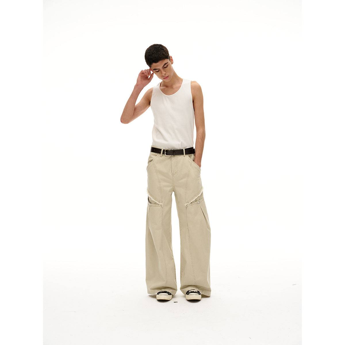 Model wearing a white tank top and beige wide-leg pants with flap knee panels, a black belt, and sneakers.